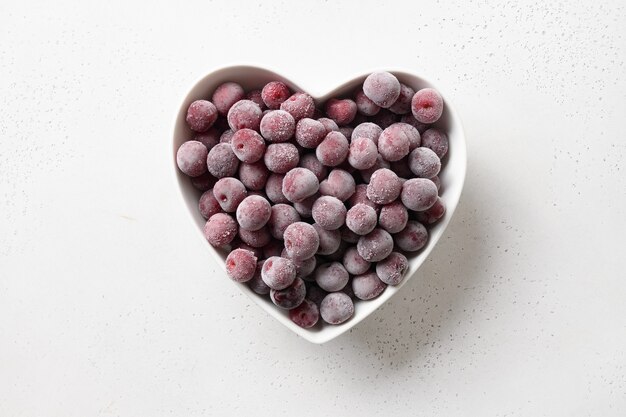 Cereza ácida roja congelada en placa con forma de corazón sobre un fondo blanco vista desde arriba