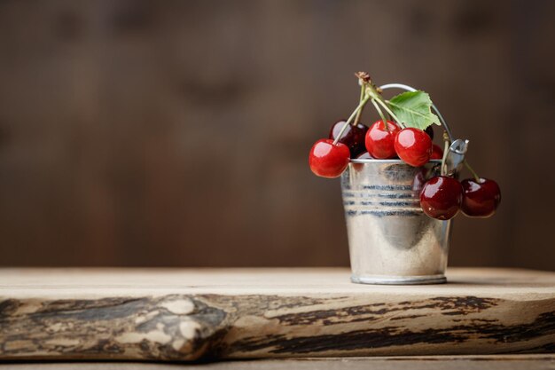 Cereza dulce en un pequeño cubo de metal decorativo sobre una tabla de madera sobre un fondo de madera marrón