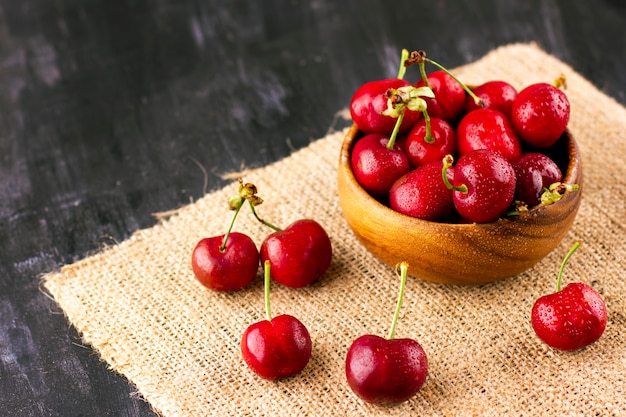 Cereza fresca en la mesa de madera negra. Bayas maduras dulces en gotas de agua