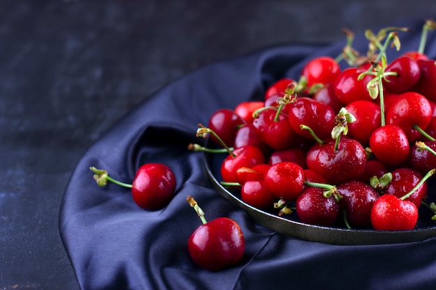 Cereza fresca sobre tela de seda oscura. Bayas maduras dulces en gotas de agua