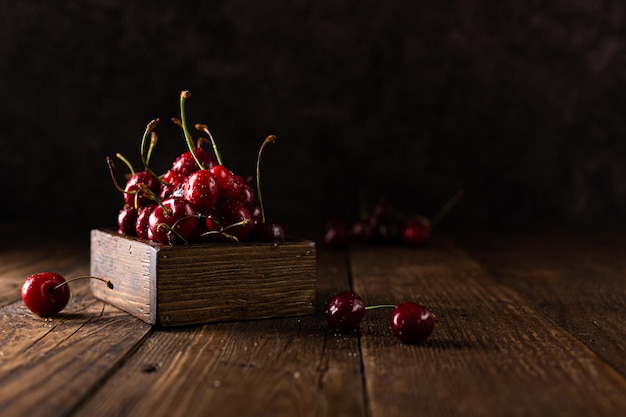 Cereza con gotas de agua en una caja de madera sobre una mesa de madera de color marrón oscuro