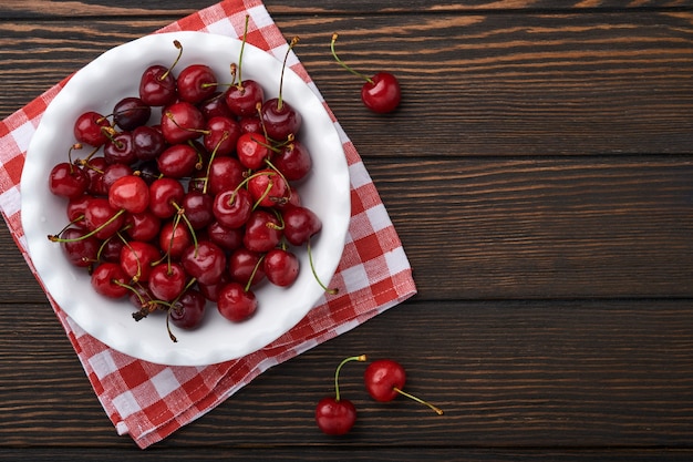 Cereza con gotas de agua en un recipiente blanco sobre la mesa de piedra de color marrón oscuro. Cerezas maduras frescas. Cerezas rojas dulces. Vista superior. Estilo rústico. Fondo de frutas