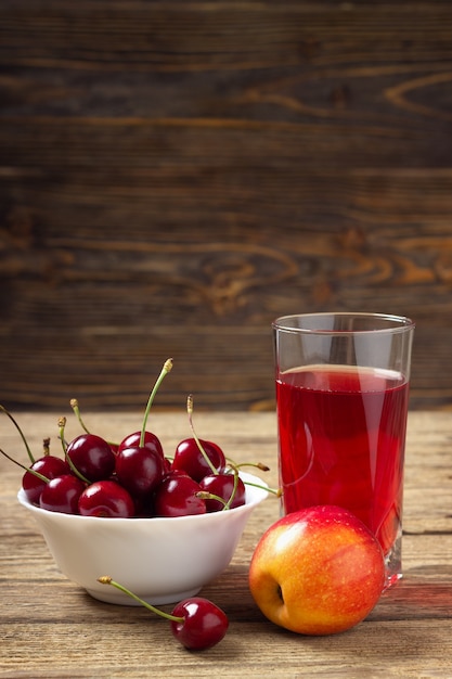 Cereza, manzana y un vaso de jugo en una mesa de madera