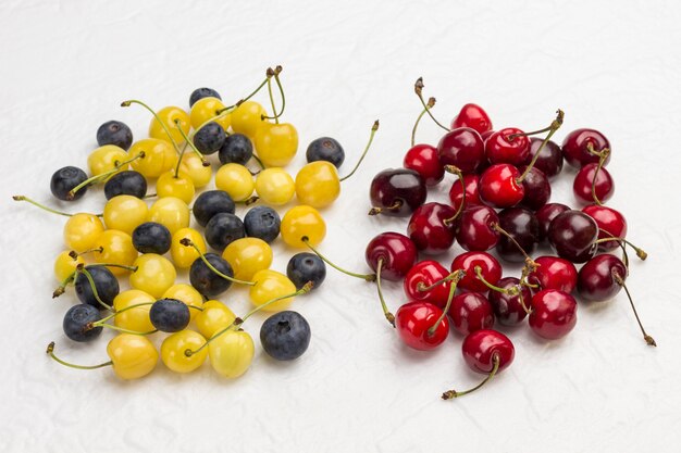 Cereza roja, cereza amarilla y arándano sobre superficie blanca