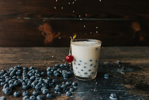 cereza roja cuelga de un vaso de arándanos flotan en un vaso transparente con leche