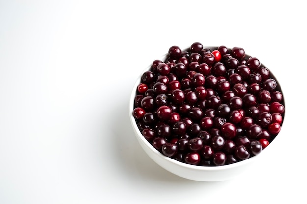 Cereza rojo oscuro en una taza blanca sobre un fondo blanco.