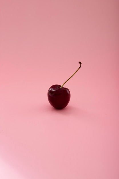 Foto cereza solitaria en el centro de un fondo rosa