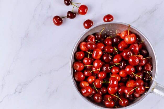 Cerezas de bayas en un recipiente colador con gotas de agua sobre una superficie blanca