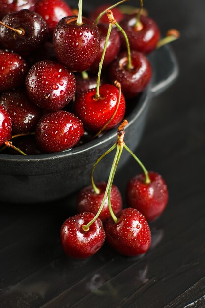 Cerezas dulces frescas con gotas de agua en un recipiente en la mesa de roca oscura.