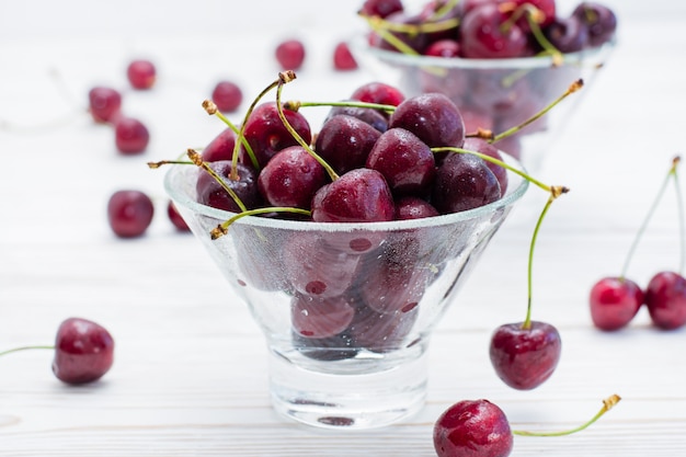 Las cerezas dulces maduras frescas en agua caen en cuencos en una tabla de madera blanca. De cerca