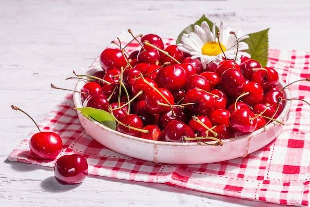 Cerezas dulces maduras frescas en un recipiente con gotas de agua. Mesa de madera blanca vieja, cerrar