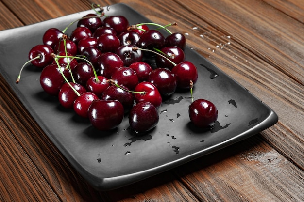 Cerezas dulces maduras y jugosas en un plato negro sobre un fondo de madera Cerezas frescas mojadas