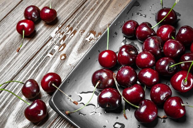 Cerezas dulces maduras y jugosas en un plato negro sobre un fondo de madera