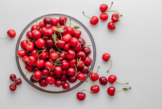 Cerezas dulces maduras en un plato colocado sobre la mesa blanca