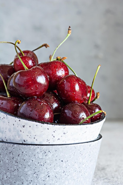 Cerezas dulces rojas maduras en un recipiente sobre un fondo gris. Frutas de temporada saludables y sabrosas.