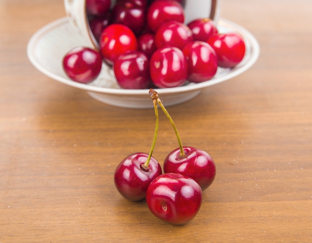 Cerezas dulces en una taza blanca sobre una mesa de madera con dos cerezas en el frente