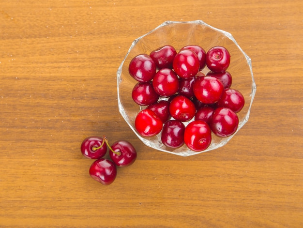 Cerezas dulces en una taza blanca sobre una mesa de madera con dos cerezas