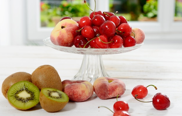 Cerezas y duraznos en un vaso de vidrio con kiwis