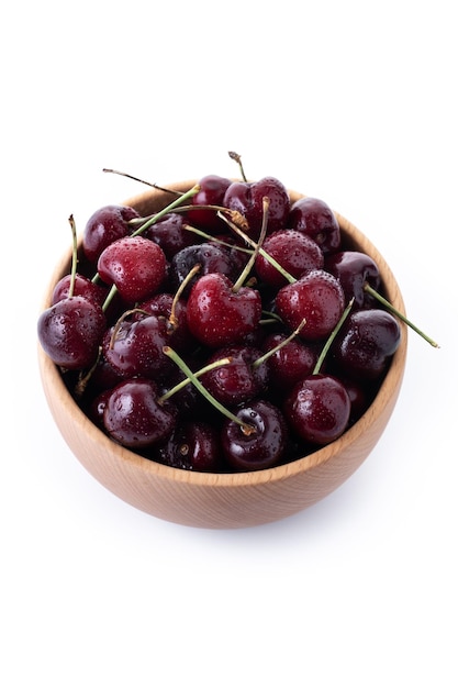 Cerezas frescas con gotas de agua en un recipiente de madera aislado sobre fondo blanco.