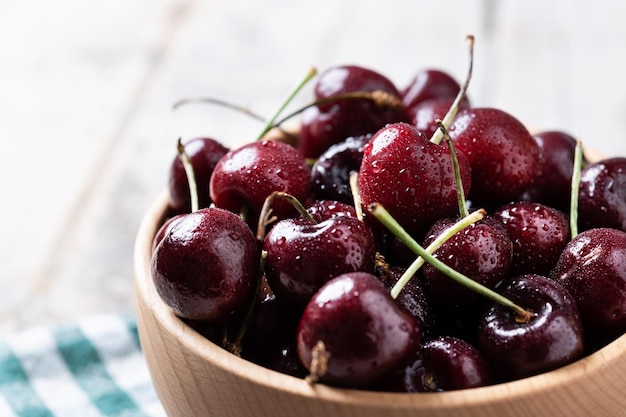 Cerezas frescas con gotas de agua en un tazón de madera sobre una mesa de madera blanca