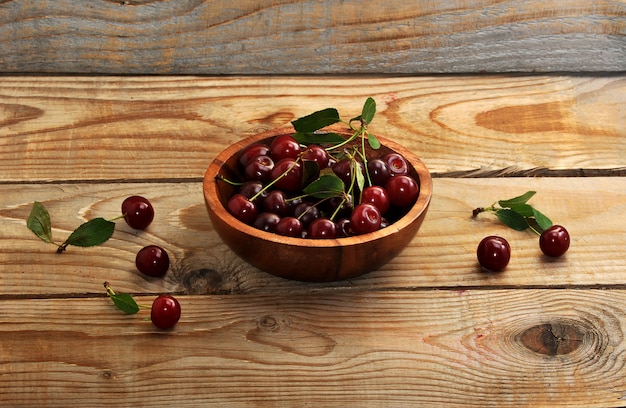 Cerezas frescas con hojas en un plato de madera sobre superficie de madera