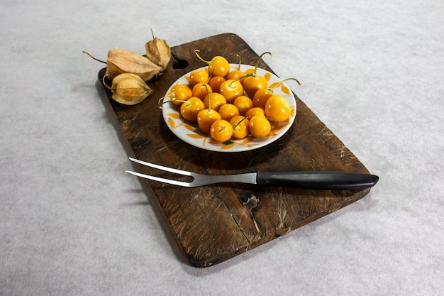 Cerezas frescas de invierno Physalis Cape gooseberry Aguaymanto Uvilla en una placa y junto a una horquilla