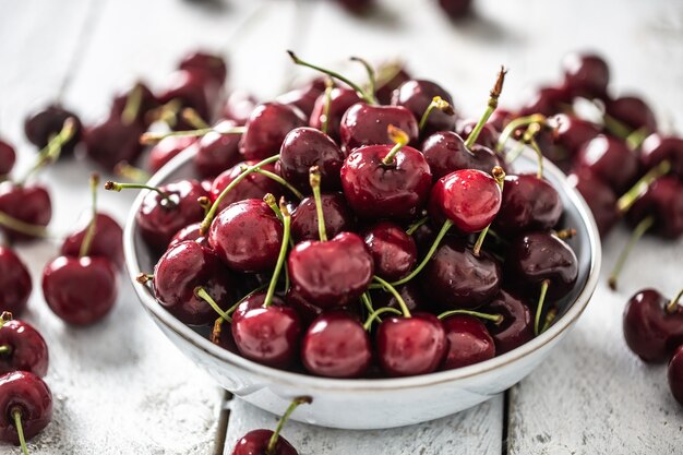 Cerezas frescas lavadas en agua limpia en un recipiente y esparcidas por todos lados.