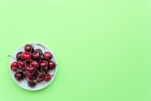 Cerezas frescas en plato blanco sobre fondo verde.