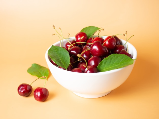 Cerezas frescas en un recipiente blanco sobre un fondo naranja con lugar para el texto