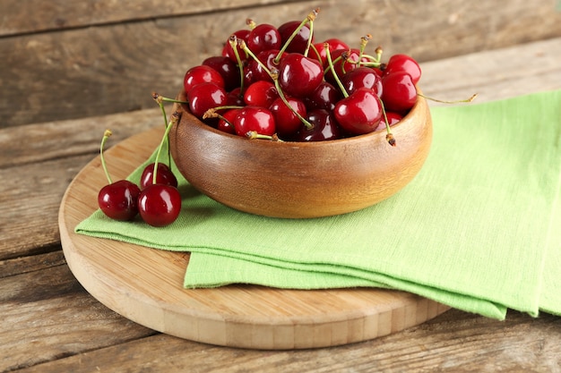 Cerezas frescas en un recipiente con una servilleta en la tabla de cortar sobre la mesa de madera