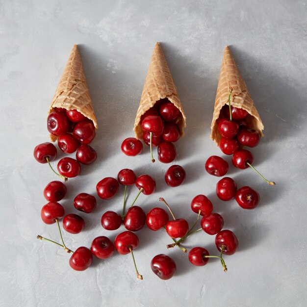 Cerezas de frutas naturales recién cosechadas en conos de galleta para tartas caseras sobre un fondo gris con lugar para el texto. Comida cruda vegetariana orgánica.