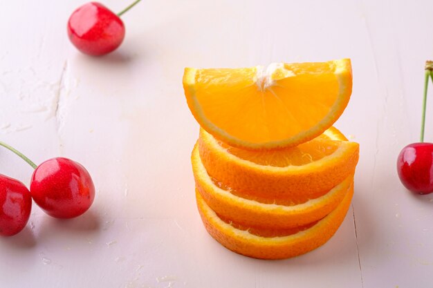 Cerezas de frutas de verano con naranjas apiladas sobre fondo blanco ángulo de visión