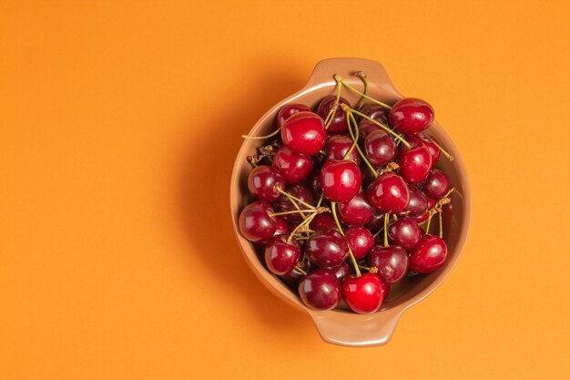 Cerezas con gotas de agua en un recipiente de arcilla sobre fondo de terracota Tazón de frutas Vista superior Comida deliciosa