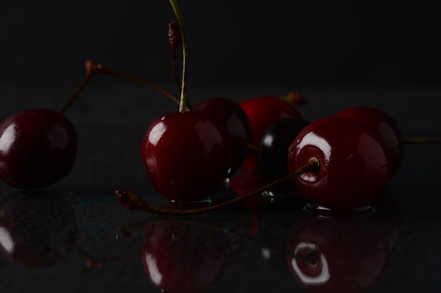 Cerezas, con gotas de agua sobre un fondo negro con reflejo