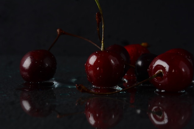 Cerezas, con gotas de agua sobre un fondo negro con reflejo