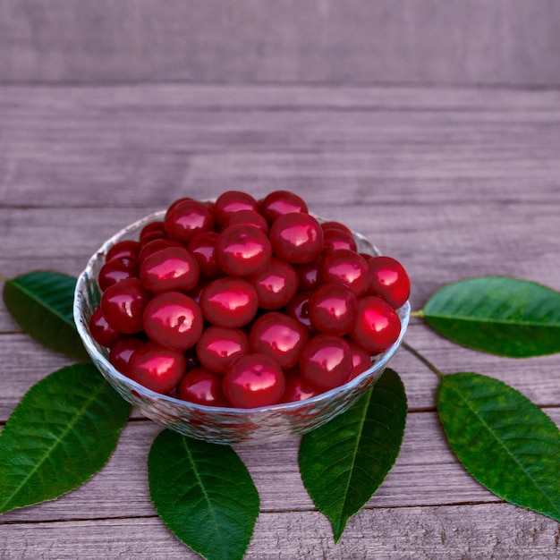 Cerezas grandes y jugosas maduras en un plato transparente sobre una mesa de madera con hojas verdes