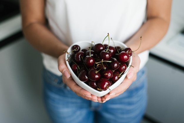 Cerezas jugosas maduras en un plato en manos de mujeres Alimentos orgánicos saludables y naturales