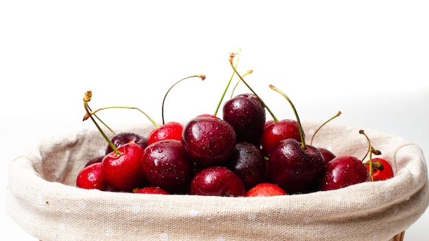 Cerezas maduras en una canasta sobre un fondo blanco.