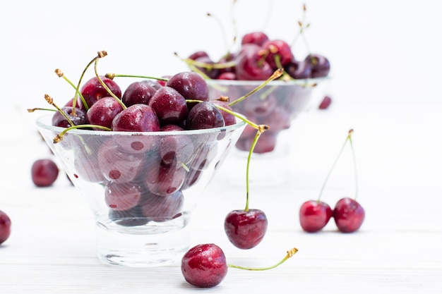 Cerezas maduras frescas en gotas de agua en cuencos sobre una mesa de madera blanca