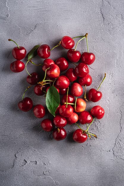 Cerezas maduras frescas con hojas verdes, bayas de vitamina de verano en piedra gris