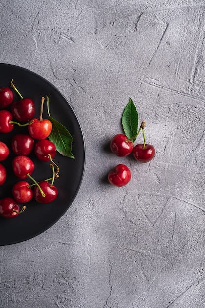 Cerezas maduras frescas con hojas verdes en placa negra