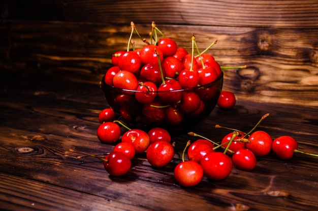 Cerezas maduras frescas en un recipiente de vidrio sobre una mesa de madera rústica