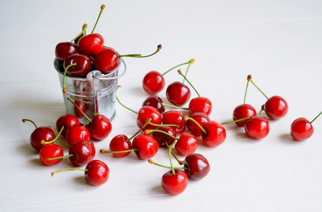 Cerezas maduras en un pequeño cubo de lata sobre madera blanca, postre sabroso y saludable