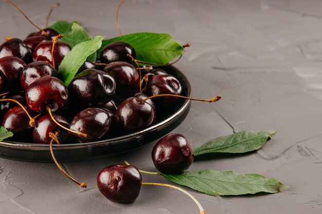 Cerezas maduras en una placa y fondo de hormigón