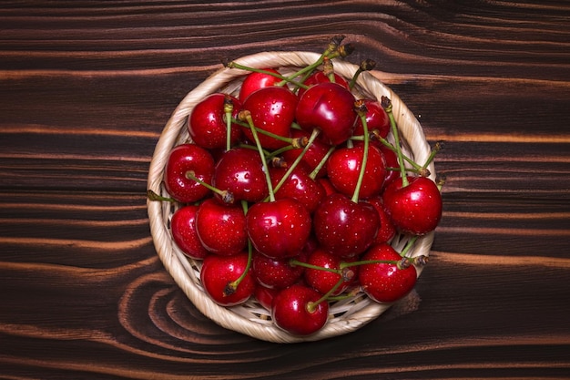 Cerezas maduras en un plato de mimbre sobre un fondo de madera Vista desde arriba