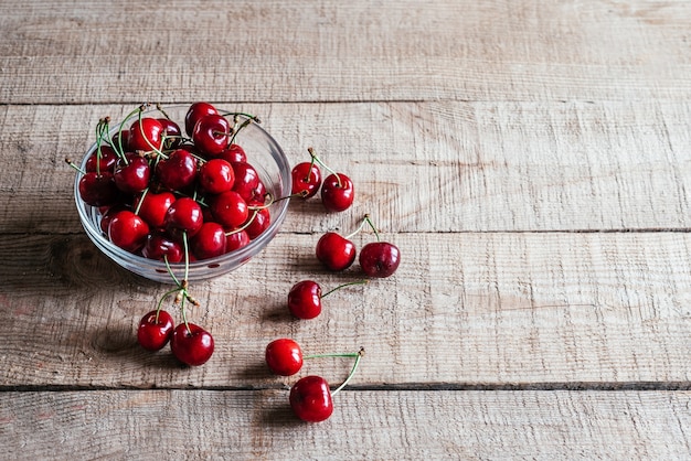 Cerezas maduras en un recipiente de vidrio sobre mesa de madera con fondo verde bokeh, frutas de verano