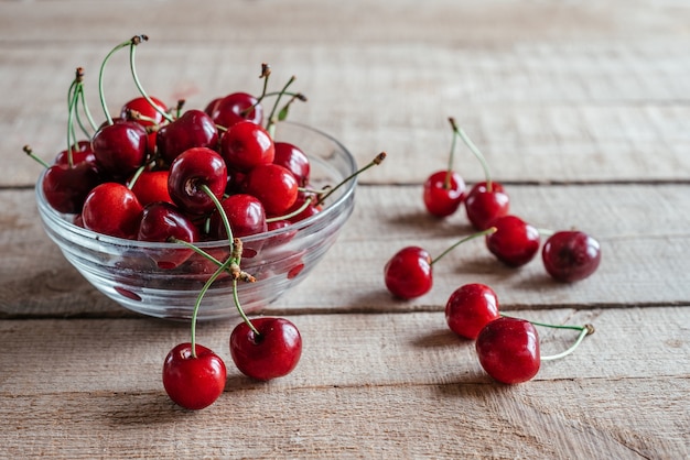 Cerezas maduras en un recipiente de vidrio sobre mesa de madera con fondo verde bokeh, frutas de verano