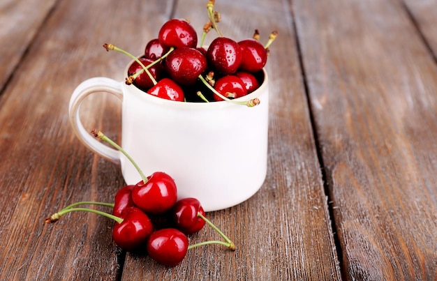 Cerezas maduras en taza sobre mesa de madera