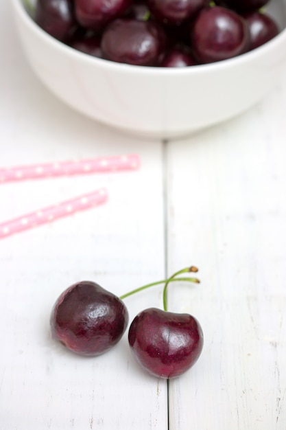 Foto cerezas negras maduras frescas en un cuenco blanco en una opinión superior del fondo de madera blanco. lay flat.