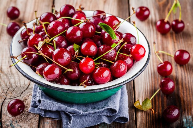 Cerezas orgánicas maduras en un bol con gotas sobre una mesa de madera